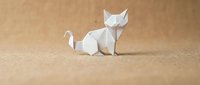 White origami cat figure folded from paper sitting on textured beige surface, minimalist Japanese paper craft art for creative projects and designs.