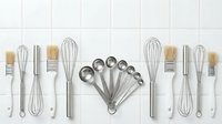 Professional kitchen utensils and baking tools arranged in organized row on white tile background for culinary cooking and food preparation needs.