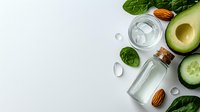 Fresh green ingredients with glass water bottle, cucumber slices, avocado, almonds and spinach leaves on light background for healthy lifestyle concept.