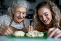 Elderly grandmother and young granddaughter sharing joyful moment while preparing dough together in kitchen, bonding through traditional family baking activity.
