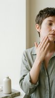 Young Caucasian woman with short hair applying face cream during morning skincare routine, natural light, wellness and beauty care concept.