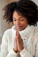 Young African American woman in white knit sweater praying peacefully with closed eyes and clasped hands, expressing spirituality and mindfulness.