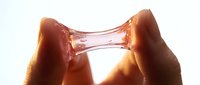 Hands holding translucent amber resin or glass material against light, showcasing material properties and light refraction for design and product visualization.