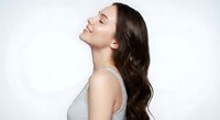 Young brunette woman with eyes closed in peaceful expression wearing gray tank top against white background for wellness and beauty concepts.
