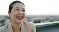 Asian woman in business attire laughing on rooftop with city skyline background. Corporate professional portrait for business, lifestyle, and success themes.