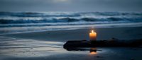 Burning candle on driftwood at twilight beach with ocean waves and wet sand reflections creating peaceful meditation atmosphere for relaxation and mindfulness.