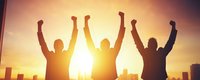 Silhouettes of three people raising arms in victory pose against dramatic sunset sky and urban cityscape, celebrating success and achievement.