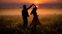 Romantic couple dancing in golden sunset field, silhouetted against warm orange sky. Man and woman enjoying intimate moment in nature during golden hour.