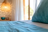 Cozy bedroom interior with turquoise bedding and woven rattan pendant lamp casting geometric shadows on wall, soft morning light through window creates peaceful atmosphere.