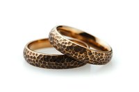 Pair of bronze wedding bands with unique hammered texture pattern on white background, showing artisanal metalwork detail and romantic symbolism.