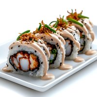 Fresh sushi roll with crispy tempura shrimp, cream sauce drizzle, and crunchy onion garnish served on white rectangular plate against light background.