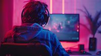 Young male gamer in denim jacket and headphones playing video games at night, illuminated by vibrant neon pink and blue lighting, perfect for gaming lifestyle and entertainment content.