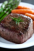 Juicy grilled beef tenderloin steak garnished with fresh rosemary and sea salt, served with baby carrots and asparagus on white plate, macro shot.