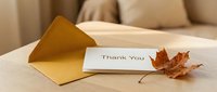 Thank you card with kraft envelope and autumn maple leaf on wooden table, warm cozy home interior, fall season greeting concept.