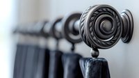 Elegant black curtain rod with decorative finial end cap featuring spiral pattern design against white wall, shallow depth of field creates artistic home decor detail.