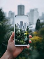 Hand holding smartphone displaying urban skyline through tropical foliage, creating contrast between nature and city architecture for environmental concepts.