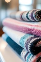 Stack of folded cozy knitted blankets in pastel pink, turquoise and navy blue colors with striped pattern, close-up view showing soft textile texture and warmth.