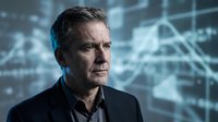 Middle-aged man with dark hair and facial stubble wearing black business attire against digital financial data backdrop. Suitable for corporate, finance, technology, and business leadership concepts.
