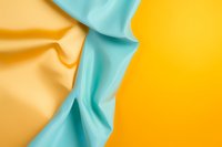 Smooth flowing fabric in contrasting turquoise blue and golden yellow creates dynamic waves and folds against solid yellow background, suitable for fashion and textile designs.