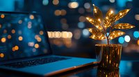 Glowing decorative leaf lamp on desk with laptop at night, illuminated by warm golden light against blurred bokeh background in moody blue tones.