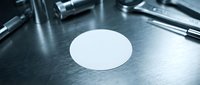 White round blank label sticker on metallic surface with medical instruments in background for product branding and identification purposes.