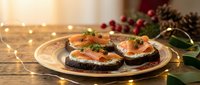 Festive smoked salmon appetizers on dark bread with cream cheese and dill, served on elegant plate with holiday decorations and warm lighting.
