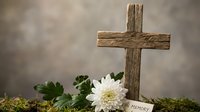 Wooden cross memorial with white chrysanthemum flower and in memory card on moss ground against soft blurred background for remembrance and grief concepts.