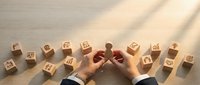 Business professional hands protecting wooden blocks with icons representing corporate strategy, risk management and leadership development concepts.