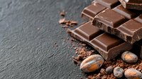 Dark chocolate bar pieces with cocoa powder and roasted cocoa beans on black stone background. Food photography for confectionery advertising and menu design.