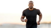Athletic African American man jogging outdoors during golden hour sunset wearing black fitness shirt for healthy lifestyle and exercise motivation.