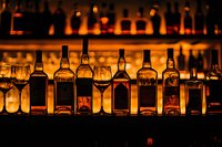 Backlit liquor bottles and glasses arranged on bar shelf with warm amber glow creating atmospheric mood for restaurant, nightclub, or hospitality industry.