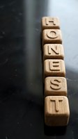 Wooden letter blocks spelling HONEST arranged in row on dark surface with shallow depth of field for business integrity and trust concepts.