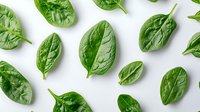 Fresh green spinach leaves scattered on white background, organic healthy food pattern layout. Clean eating and nutrition concept. Isolated.