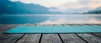 Wooden dock with turquoise painted boards overlooking calm mountain lake at dawn, serene landscape for travel and nature designs.
