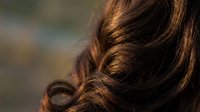 Close-up of glossy brown curly hair with warm highlights showing texture and shine for beauty and haircare concepts.
