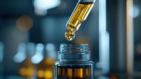 Amber liquid dropping from glass dropper into bottle on dark background with bokeh effect. Aromatherapy oil or medical tincture concept for wellness and healthcare.
