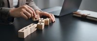 Business professional arranging wooden blocks in sequence on office desk, representing strategic planning and problem-solving in corporate environment.