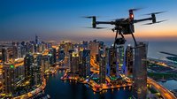 Drone flying over illuminated city skyline at sunset with modern skyscrapers and waterfront marina creating stunning aerial photography perspective for commercial use.