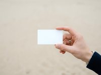 Caucasian hand holding blank white business card against neutral beige background, suitable for branding, corporate identity, and mockup design projects.