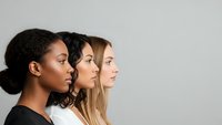 Three diverse women in profile view showcasing different ethnicities and hairstyles against neutral background for beauty and diversity concepts.