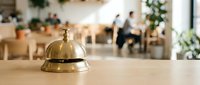 Golden brass service bell on wooden counter in modern restaurant interior with blurred dining area background for hospitality industry.