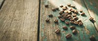 Roasted coffee beans scattered on rustic wooden surface with weathered teal paint, overhead view for beverage, cafe, and food industry design projects.