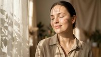 Young woman with closed eyes enjoying warm sunlight streaming through window in peaceful morning meditation moment at home.