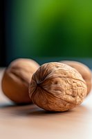 Fresh whole walnuts on wooden surface with soft green background blur, macro food photography showing detailed texture of nutshell in natural lighting.