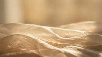 Soft golden sunlight illuminates rumpled bed sheets creating warm shadows and highlights across fabric texture for cozy bedroom interior design.