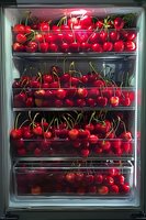 Fresh ripe red cherries with stems arranged in refrigerator drawers, bright and glossy fruit filling multiple transparent compartments for food storage.