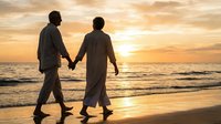 Romantic couple holding hands walking on beach at golden sunset with ocean waves and dramatic sky creating peaceful moment for love and relationship concepts.