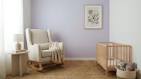 Nursery room with lavender walls, wooden rocking chair with beige upholstery, crib, and botanical wall art for baby interior design projects.