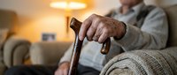 Senior man hands holding wooden walking cane at home, elderly care and mobility assistance concept for healthcare and aging support.