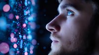 Young Caucasian man profile view with beard against dark background with blue and pink bokeh lights creating magical atmosphere. Contemplative expression in dramatic lighting.